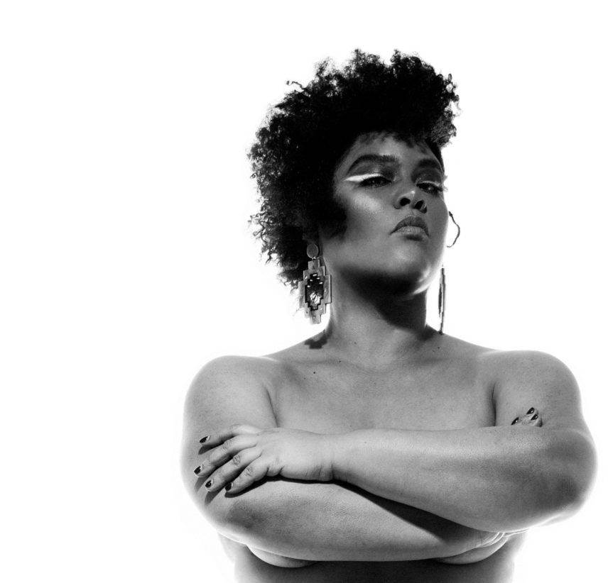 A black and white image of the upper half of Candy Bowers, standing nude with her arms crossed over her chest