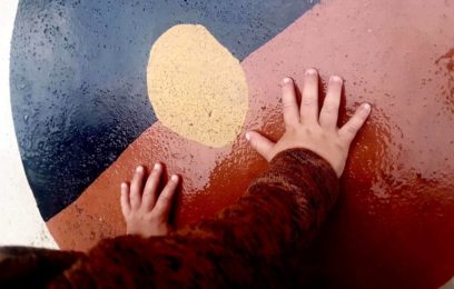 A child's hands touching the Aboriginal flag which has been painted on concrete