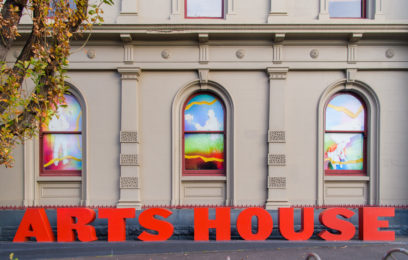 Image by Sarah Walker. Eugenia Lim - All of this is temporary - Three arched windows on a cream brick building. The windows have colourful artwork in them and there are large red letters out the front of the building that say "Arts House"