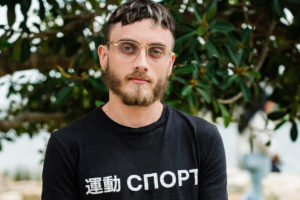 Joel Sherwood-Spring photograph of a man with a beard and thin rimmed glasses with his hands together in front of some trees.jpg