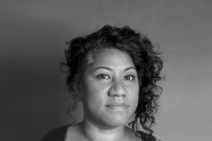 Latai-Taumoepeau-headshot-by-Stelios-Papad a woman with dark curly hair looking directly at the camera in a black vest