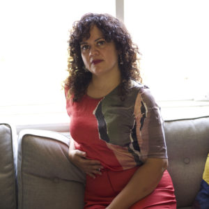 a woman in red pants and colourful top with black curly hair sitting on a sofa