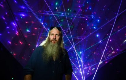 artist Robin Fox standing in a dark room with his laser artwork